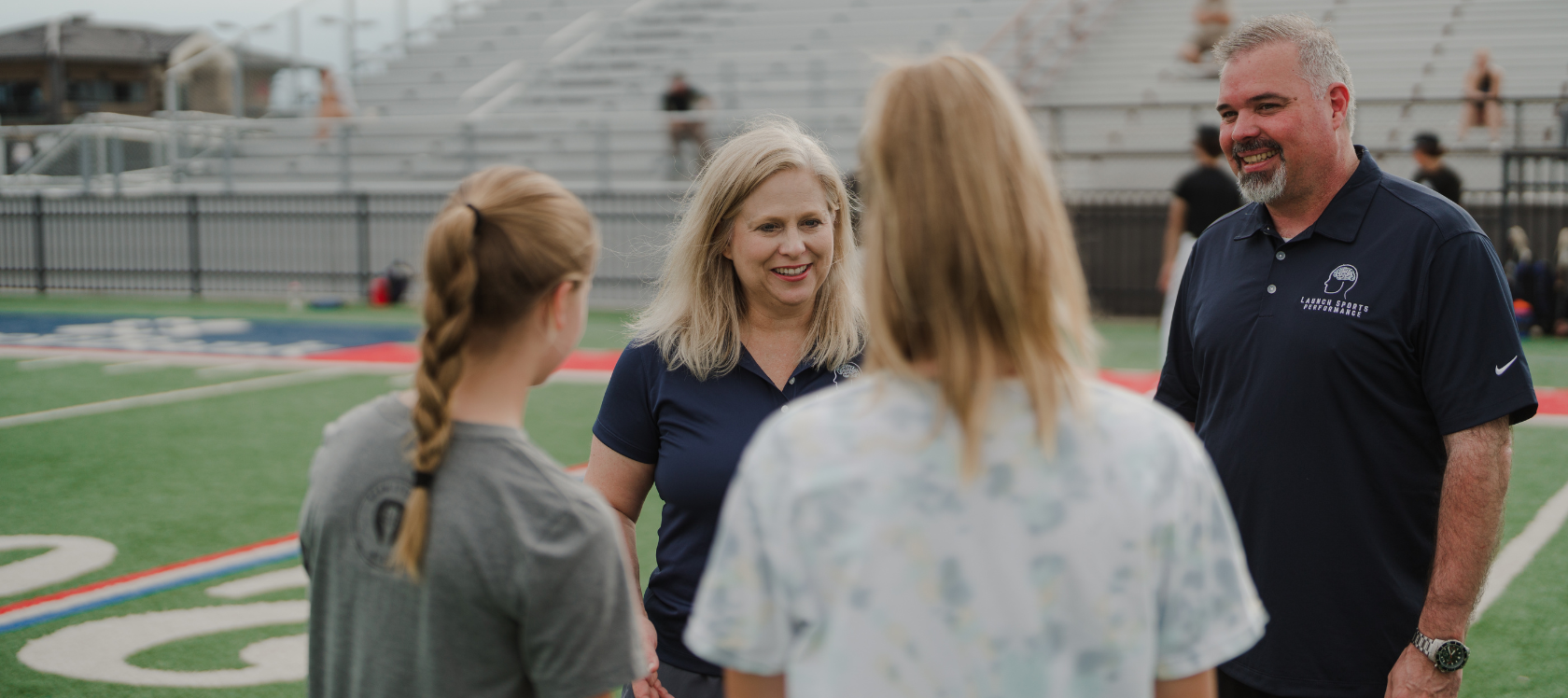 two mental game coaches smiling while talking to athletes on a football field