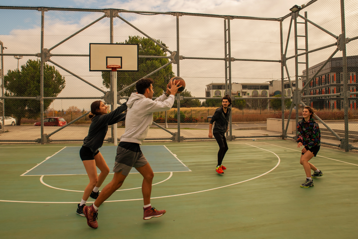 Four high schoolers on a community basketball court playing basketball.