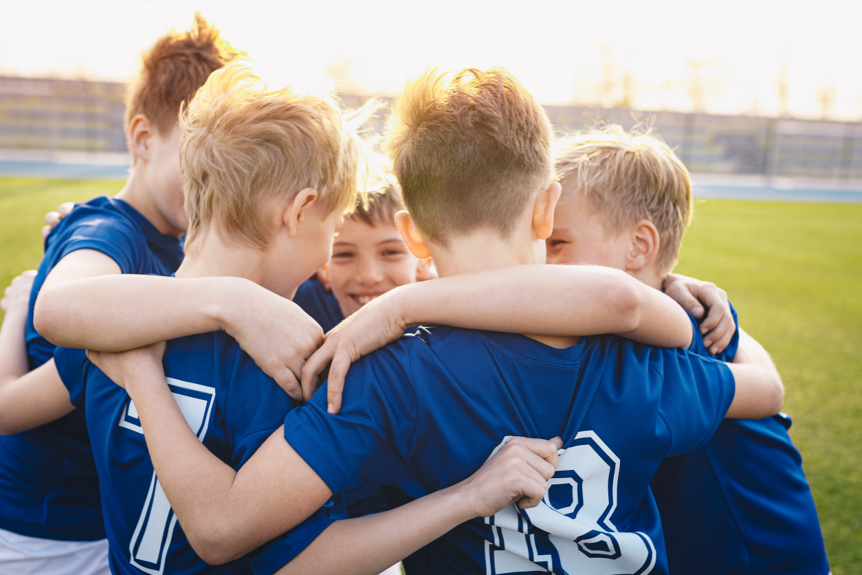 Group of boys smiling and huddling together, in soccer uniforms