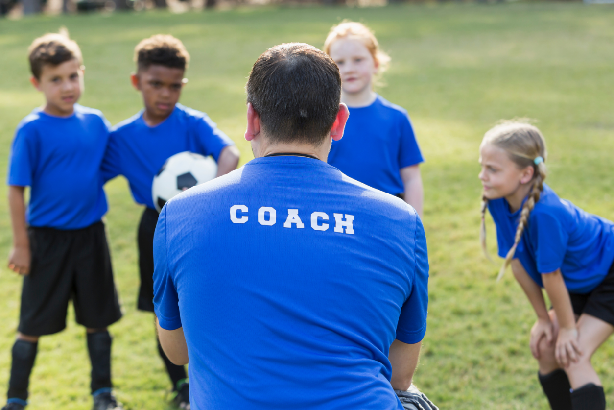 A behind shot of a coach teaching a group of kids playing soccer