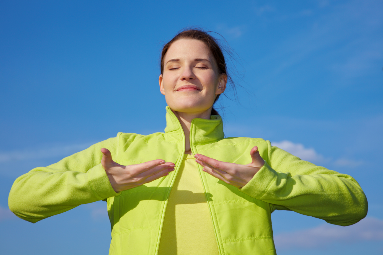 Woman in a lime green jacket holding her hands up and breathing deeply in