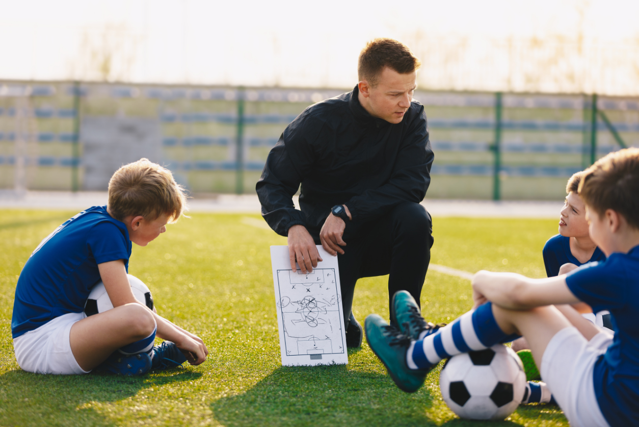 Male Coach teaching young soccer students strategy.