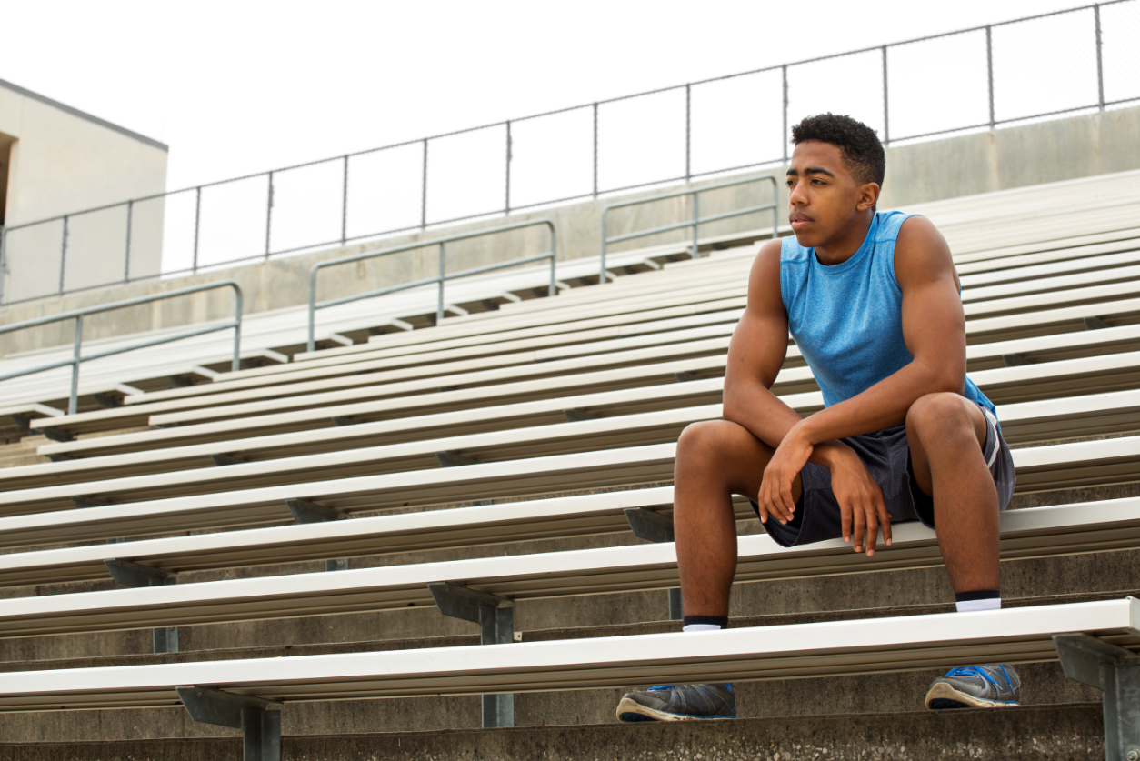 Teenage male athlete sits in the bleachers alone.