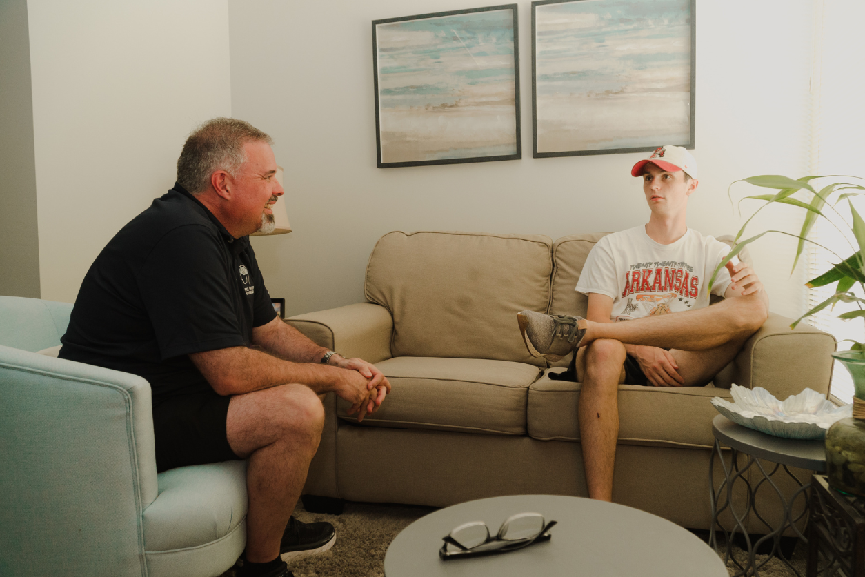 A therapist talks with a young athlete in a white t-shirt with a white ballcap.