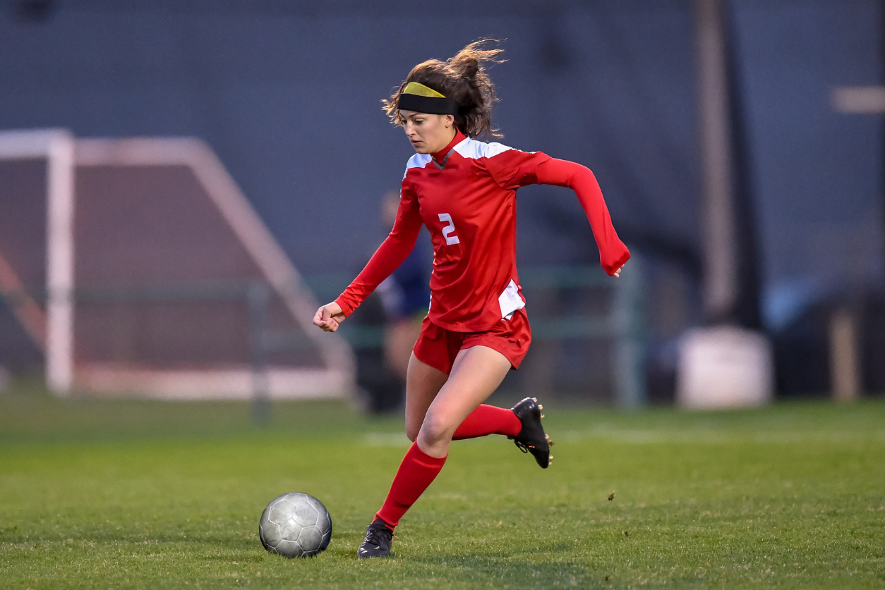 A young woman soccer player in a red uniform kicks the soccer ball.