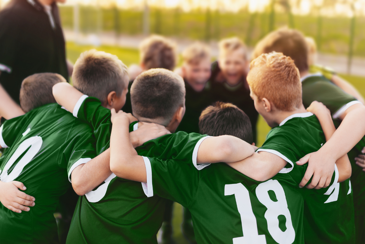 A team of boys playing a sport in green jerseys huddle together with arms around each other.