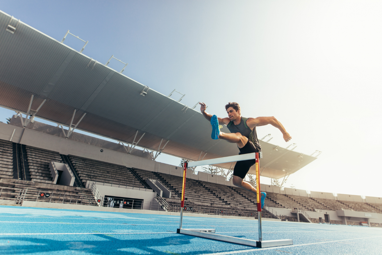 A male hurdle runner jumps a hurdler on the track.