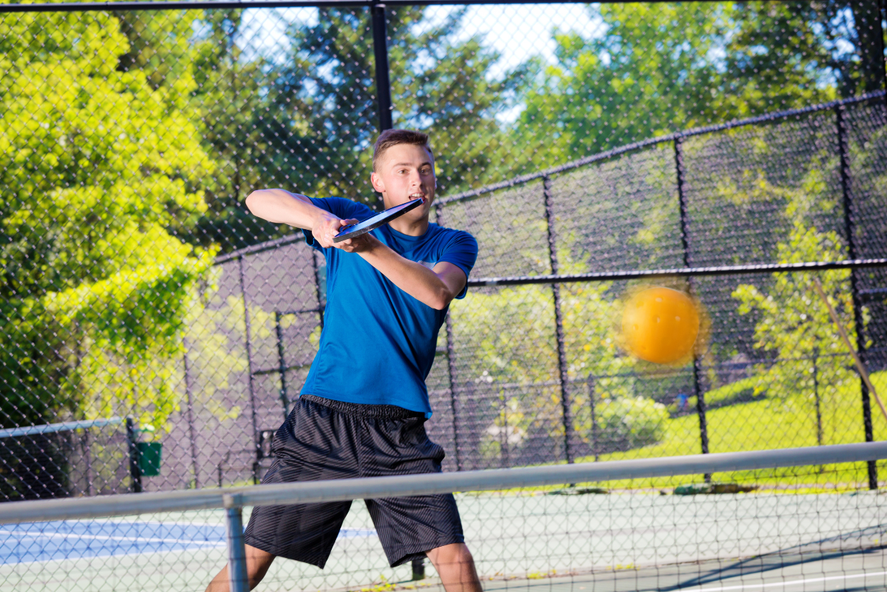 A young male wearing a blue shirt hits a ball across a net with his racket.