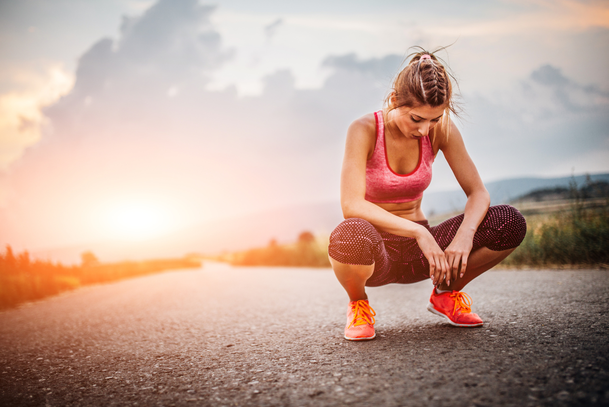 A female athlete crouches tiredly on the road with the sunset behind her.