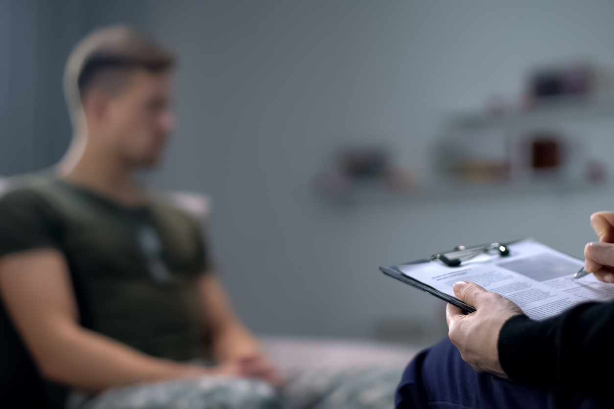 A male athlete sits forward while meeting with a professional with a clipboard, writing on a paper.