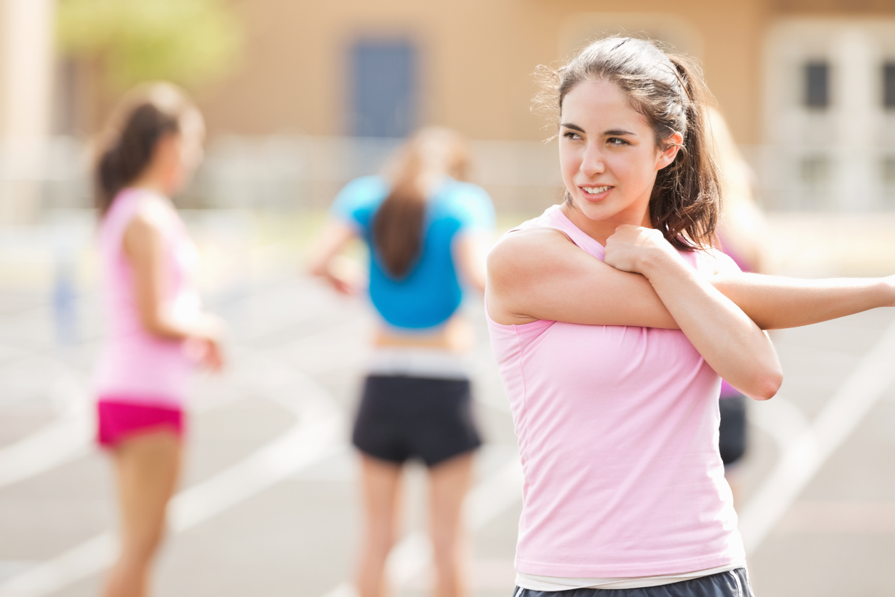 A brown-haired athlete in a pink tank top stretches on a track.